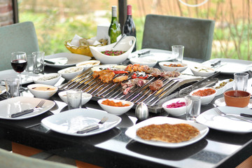 Traditional Cypriot meze and mix meat and chicken kebab table with charcoal barbecue on the table for self cooking during the eating time