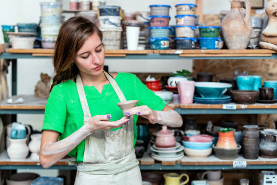 Master class concept. Beautiful attractive dreamy charming nice lady in her workwear she stand against wooden shelf with utensil stuff background inside workspace studio check quality of ceramics cup