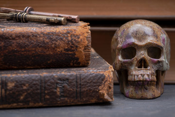 Pile of antique hard cover books, old vintage metallic keys and carved skull on natural stone background