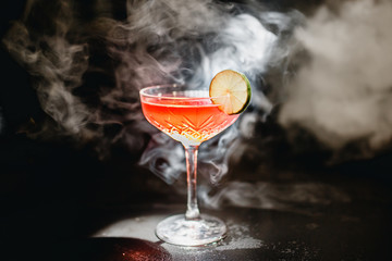Alcoholic cocktail Greyhound, with vodka, liqueur, grapefruit juice and ice, black background, all in smoke, garnished with lemon