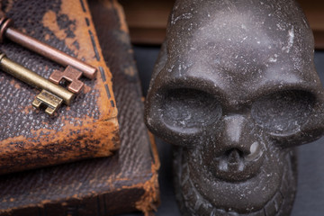 Pile of antique hard cover books, old vintage metallic keys and carved skull on natural stone background