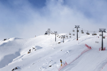 Fototapeta na wymiar Snowy ski slope and ski-lift at ski resort at sunny winter evening
