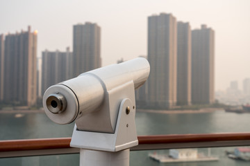 Metal optical telescope on deck of cruise boat looking misty buildings of Qingdao