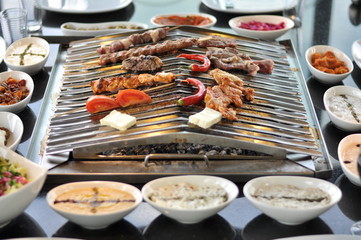 Traditional Cypriot meze and mix meat and chicken kebab table with charcoal barbecue on the table for self cooking during the eating time