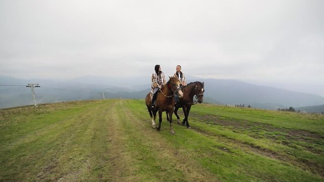 Beautiful couple ride horses in mountains in cloudy weather