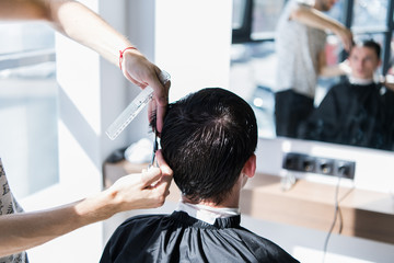 Close up of a haircut at the hair saloon. Barber triming a client's hair with a scissors.
