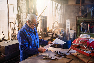Senior man in his workshop repairing an old fashioned pedal car 
