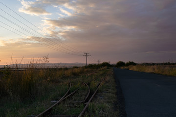 Obraz premium An asphalt road, a train line and power line with and power pylons through the field.