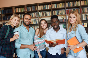 Portrait of multiethnic diverse friends pupils looking at page of interesting book in college library