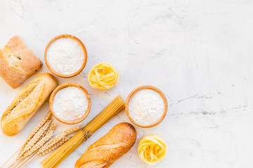 Homemade fresh bread and pasta near flour in bowl and wheat ears on white stone background top view copy space