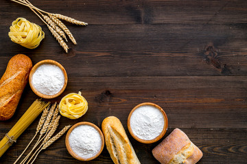 Homemade fresh bread and pasta near flour in bowl and wheat ears on dark wooden background top view copy space