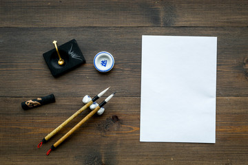 Lesson of calligraphy concept. White blank sheet for lettering near writing accessories on dark...