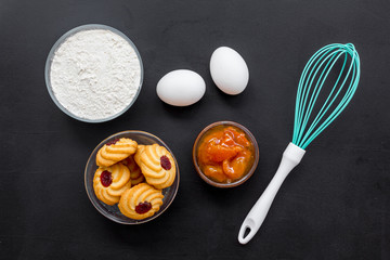 Cook cookies at home concept. Ingredients and instruments for make cookies. Fresh cookies near flour, eggs and whisk on black background top view