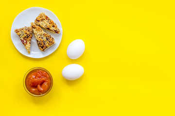 Ingredients for homemade cookies. Fresh cookies near jam, eggs on yellow background top view copy space