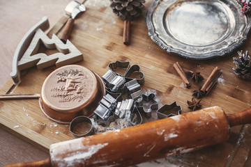 Christmas gingerbread cookies with metal cutters on rustic table with wooden rolling pin, cinnamon ,anise, cones, christmas decorations, vintage plate. Atmospheric stylish image