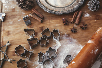 Christmas gingerbread cookie metal cutters on rustic table with wooden rolling pin, cinnamon ,anise, cones, christmas decorations, vintage plate. Atmospheric stylish image, winter holidays