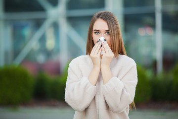 Cold and flu. Young attractive girl, caught a cold on the street, wipes her nose with a napkin