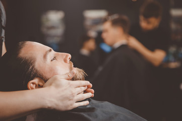 Barber applies shaving foam on man beard.