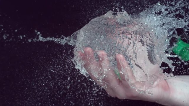 BB gun shot at water balloon makes it burst in hand of person.
