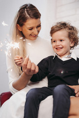 Mother and sun sitting on a chair and firing sparklers in Christmas decorated studio