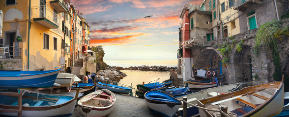 Straße mit Fischerbooten und Blick auf die Bucht im Dorf Riomaggiore bei Sonnenuntergang. Ligurien, Italien