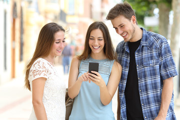 Three friends checking smart phone content in a street