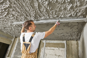 Plasterer smoothing plaster mortar on ceiling with screeder