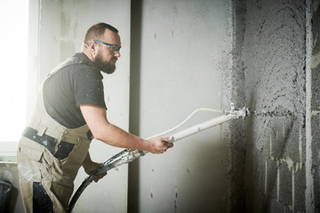 Plasterer using screeder spraying putty plaster mortar on wall - obrazy, fototapety, plakaty