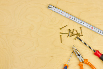 screwdriver and pliers with screws lie on the plywood. copy space. DIY concept.