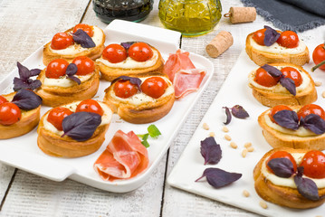 bruschetta with basil leaves and red cherry tomatoes on white basalt board on white wooden background