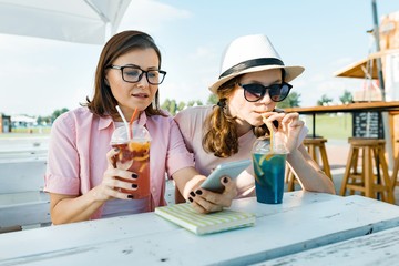 Happy mother and teen daughter talking and smiling. Parents with a kid in a summer outdoor cafe enjoying cold drinks on a hot summer day