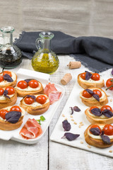 bruschetta with basil leaves and red cherry tomatoes on white basalt board on white wooden background