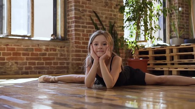 A young charming ballerina in black tutu making twine in the dancing hall. Slim dancer ballerina in black tutu practicing stretching twine at dance school
