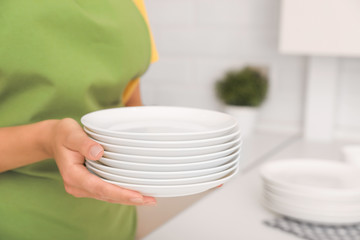 Woman holding stack of clean dishes in kitchen, closeup. Space for text