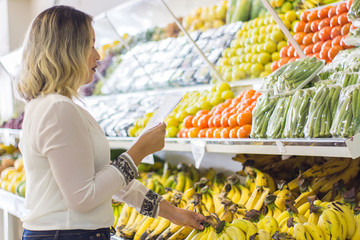 young woman holding shopping list with fruits background in supermarket