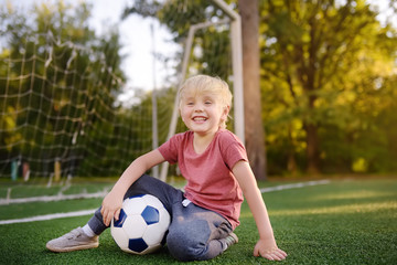 Little boy having fun playing a soccer/football game on summer day. Active outdoors game/sport for children.
