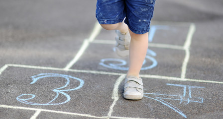 Closeup of little boy's legs and hopscotch drawn on asphalt