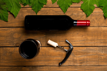 Wine bottle opener glass stoppers and vine leaves on wooden background. Top view with copy space.