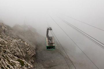 Cable car climbing a mountain from foggy valley.