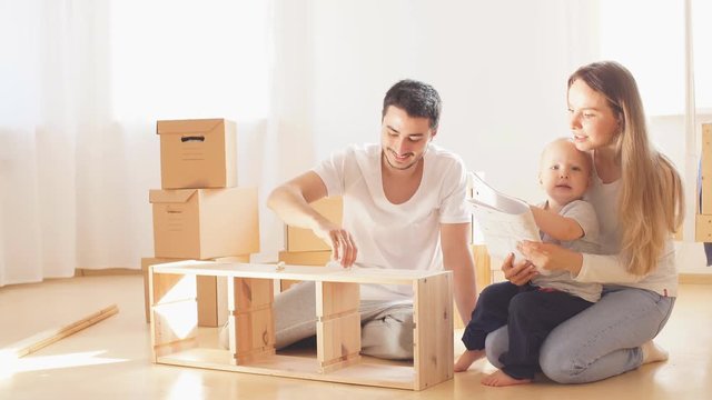 family with little boy reading instruction and assemble furniture together at living room of new apartment pile of moving boxes on background