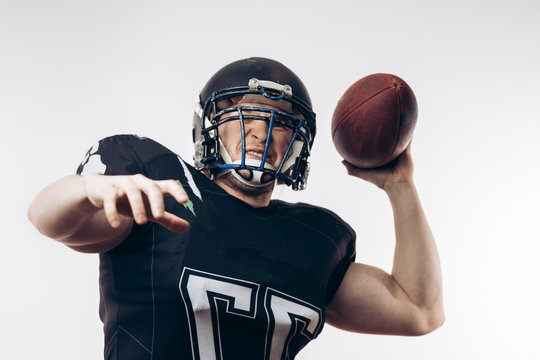 Forward Man In Black Protective Uniform Throwing A Ball In A Professional American Football Game, Isolated Studio Shot Over White Background. Sport Concept