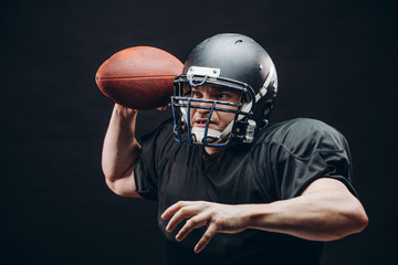Forward man in black protective uniform throwing a ball in a professional American football game, isolated studio shot over white background. Sport Concept