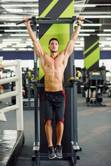 Fototapeta na wymiar Strong attractive man does pull-up on the crossbar during training in the modern gym. Front view.