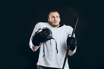 Fototapeta premium Frightened hockey player in protective white uniform holding white hard hat and hockey stick looking aside with anxious or alarmed expression, isolated over black background