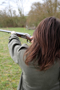 young woman hunter in action, aiming with her vintage shotgun.