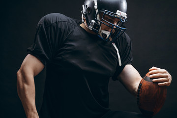 Sport concept. American football sportsman player in black sports outfit on black background with...