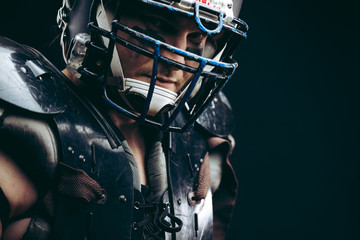Portrait of american football player with ball wearing helmet and protective shields looking at...