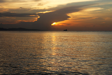 Sunset over the bay, Montego Bay, Jamaica. The sky is golden color, the hillside is in shadow, and a  strip of yellow, gold sunlight is reflective off the water.
