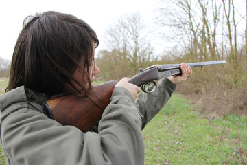 young woman hunter in action, aiming with her vintage shotgun.