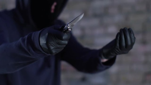 Gagster in mask and hood threatening with knife demanding money, danger